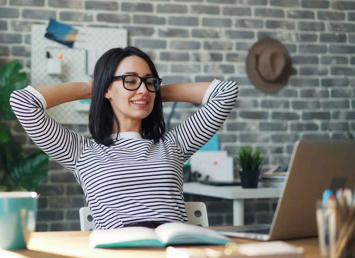 a woman sitting at a desk with her hands behind her head